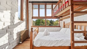 Habitación con literas, ropa de cama blanca, vistas a la vegetación y una pared de ladrillo.