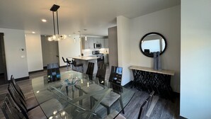 Un espace repas moderne avec une table et des chaises en verre, une cuisine en arrière-plan et un miroir rond accroché au mur.