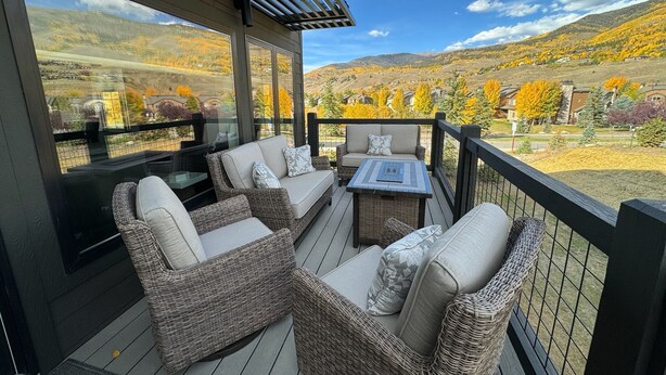 Un espace extérieur aménagé, abrité et doté de mobilier en osier, offrant une vue sur un paysage montagneux.