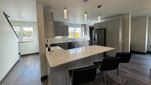 Une cuisine moderne dotée d’un îlot central, de tabourets de bar, de luminaires suspendus et offrant une vue sur l’extérieur.