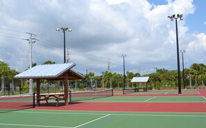 An outdoor tennis court with a wooden pavilion, a picnic table, and multiple tennis courts.