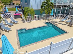A rectangular pool with a white fence, lounge chairs, and umbrellas.