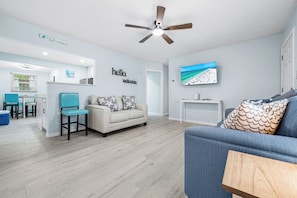 A modern living room with a ceiling fan, a sofa, a coffee table, and a TV mounted on the wall.