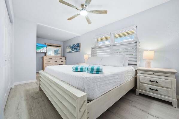 A bedroom with a bed, nightstands, a ceiling fan, a TV, and artwork on the wall.