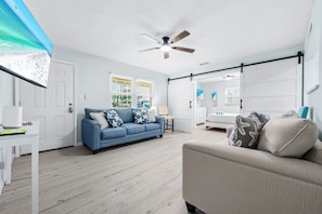 A modern living room with a blue sofa, a beige armchair, a ceiling fan, and a sliding barn door.