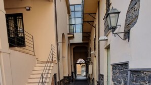 Ein schmaler, mit Fliesen ausgelegter Gang mit einer Treppe links und einer Steinwand rechts.
