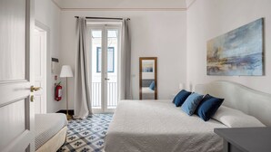 Ein Hotelzimmer mit Bett, Nachttisch, Lampe, Feuerlöscher und Blick durch eine Tür nach draußen.