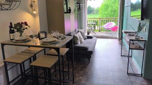 A dining area with a table set for four, a sofa, and a balcony with a view of greenery. - Flat*** near Beaune center, quiet, swimming pool, sauna, golf (Levernois)