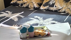 A neatly made bed with a tropical leaf pattern bedspread, a tray with cookies and a teapot, and two cups. - Flat*** near Beaune center, quiet, swimming pool, sauna, golf (Levernois)