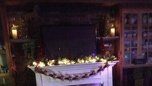 Una sala de estar acogedora con chimenea, un televisor montado encima y un árbol de Navidad con luces.