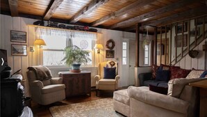 Una sala de estar acogedora con vigas de madera, una chimenea, un sofá, sillones y una mesa de comedor.