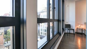 Moderni hotellihuone, jossa on suuret ikkunat, puulattia ja pieni pöytä tuolilla.