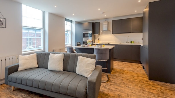 Una cocina moderna con armarios oscuros, una isla central y un comedor con sofá gris y cojines blancos.