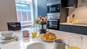Una preparación para el desayuno con croissants, zumo de naranja y una cafetera sobre una encimera de cocina.