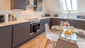 A modern kitchen with dark cabinets, a built-in oven, and a glass dining table with chairs. - 5C Charming Town Centre Apartment With Roof Top Views - Pass the Keys (Shrewsbury)