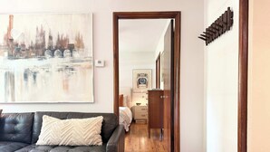 A living room with a dark leather sofa, a painting of a bridge, a wooden floor, and a hallway leading to a bedroom. - the hideaway: w/pool, hot tub, relaxing courtyard (Houston)