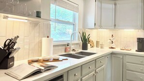 A modern kitchen with white cabinets, a built-in dishwasher, a window with blinds, and a coffee maker on the counter. - the hideaway: w/pool, hot tub, relaxing courtyard (Houston)