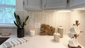 Eine Küche mit weißen Schränken, einem Topf mit Pflanze, einer Kerze, einer Holzskulptur und einem Becherhalter.