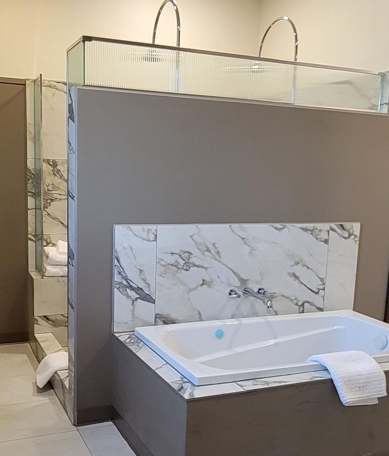 A modern bathroom with a marble-tiled shower enclosure, a glass partition, and a freestanding bathtub with a towel.