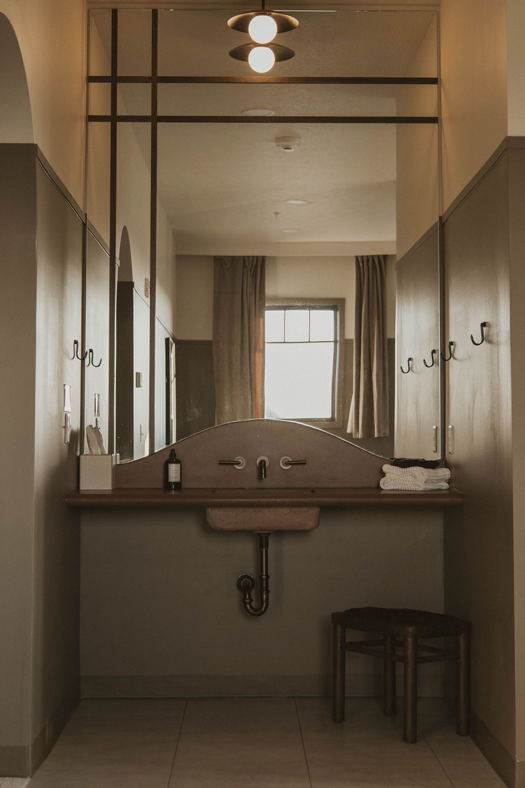 A bathroom with a wooden vanity, a mirror, a sink, a towel rack, and a small stool.