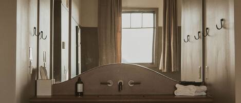 A bathroom with a wooden vanity, a mirror, a sink, a towel rack, and a small stool.