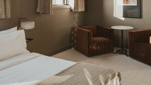 A hotel room with a large bed, a desk, two armchairs, a small table, and a window with curtains. - The Atlee Suites (Berlin)