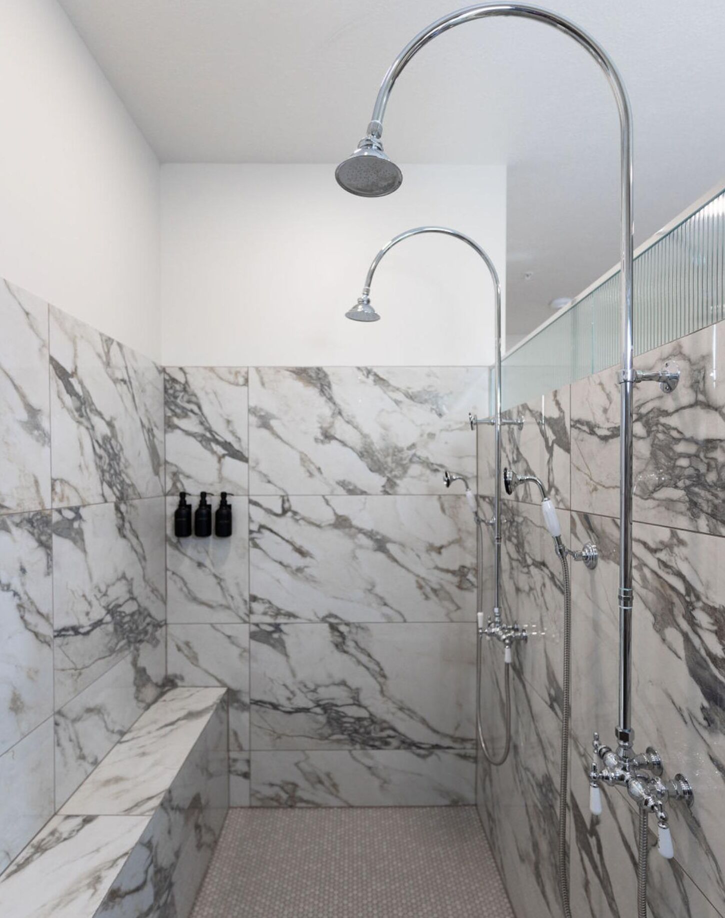 Une douche moderne dotée d’une pomme de douche incurvée, de murs en marbre et d’un banc.