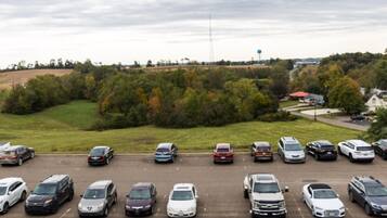 A parking lot with various vehicles, surrounded by greenery and a water tower in the distance.