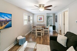A living room with a black sofa, a wooden dining table, and a ceiling fan. - Clean & Modern Apt DT Libertyville near Naval Base (Libertyville)