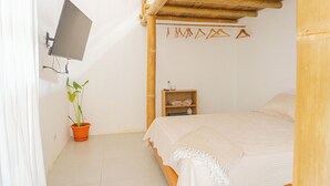A bedroom with a bed, a TV mounted on the wall, a potted plant, and a shelf with towels. - Casa Perezoso-Private pool- 800m from the beach. (Bahia Ballena)