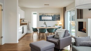 A modern kitchen with white cabinets, a wooden dining table, and teal chairs. - Ferienhaus Sonnenweg 32 - Sauna, Garten und Seeblick Inklusive (Diemelsee)