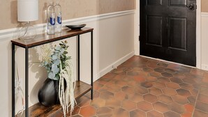 A hallway with a black door, a round mirror, a small table with a lamp and bottles, and a vase with plants. - Forest Retreat - BBQ - Game Room (Shreveport)