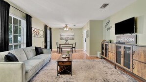 A living room with a sofa, coffee table, dining table, and chairs. - Forest Retreat - BBQ - Game Room (Shreveport)