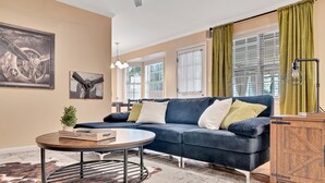 A living room with a dark blue sofa, a round coffee table, and a wooden cabinet. - Forest Retreat - BBQ - Game Room (Shreveport)
