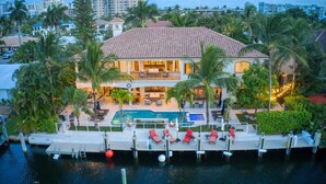 A large house with a swimming pool, dock, and palm trees.