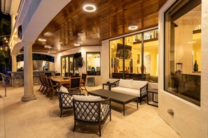 Une vaste terrasse extérieure dotée d’un plafond en bois, d’un coin repas avec des chaises et une table, ainsi que d’un canapé.