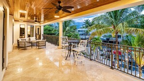 A covered outdoor area with a wooden ceiling, ceiling fan, and a seating arrangement with chairs and a table.