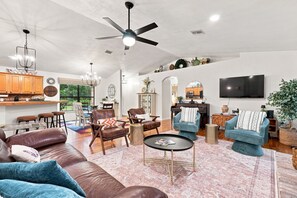 A spacious living room with a brown leather sofa, blue armchairs, a coffee table, and a ceiling fan.