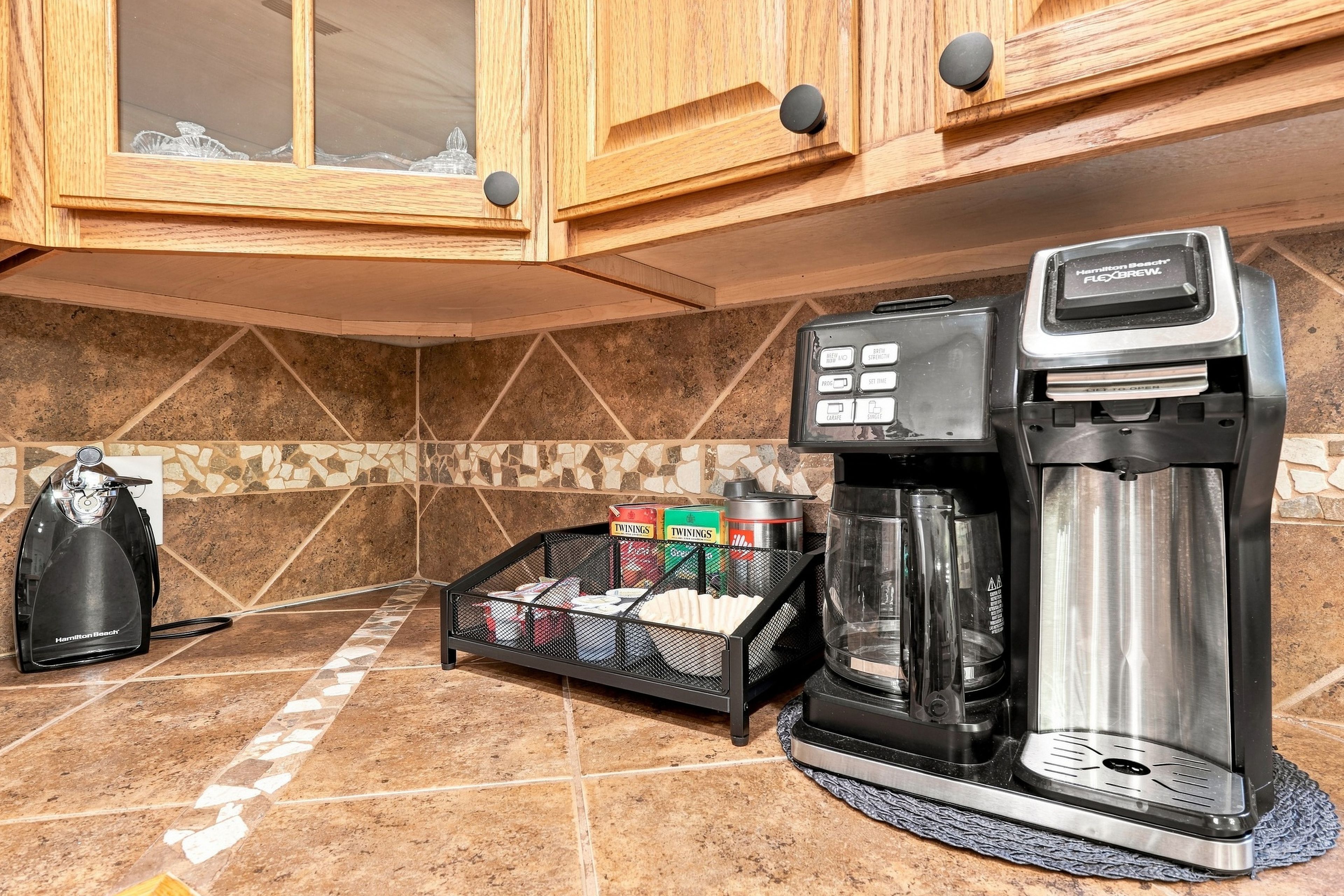A kitchen with a coffee maker, a coffee pot, and a basket of Twinings tea boxes.