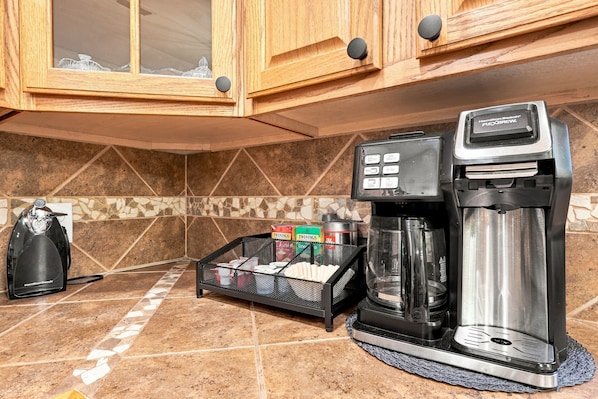 A kitchen with a coffee maker, a coffee pot, and a basket of Twinings tea boxes.