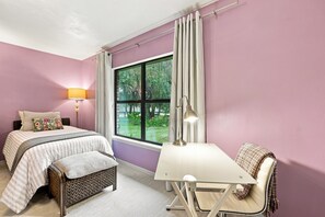 A bedroom with a bed, a desk, a chair, a lamp, and a window with curtains.
