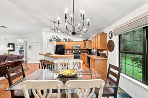 A modern kitchen with wooden cabinets, a central island, and a dining area with a glass table and chairs.