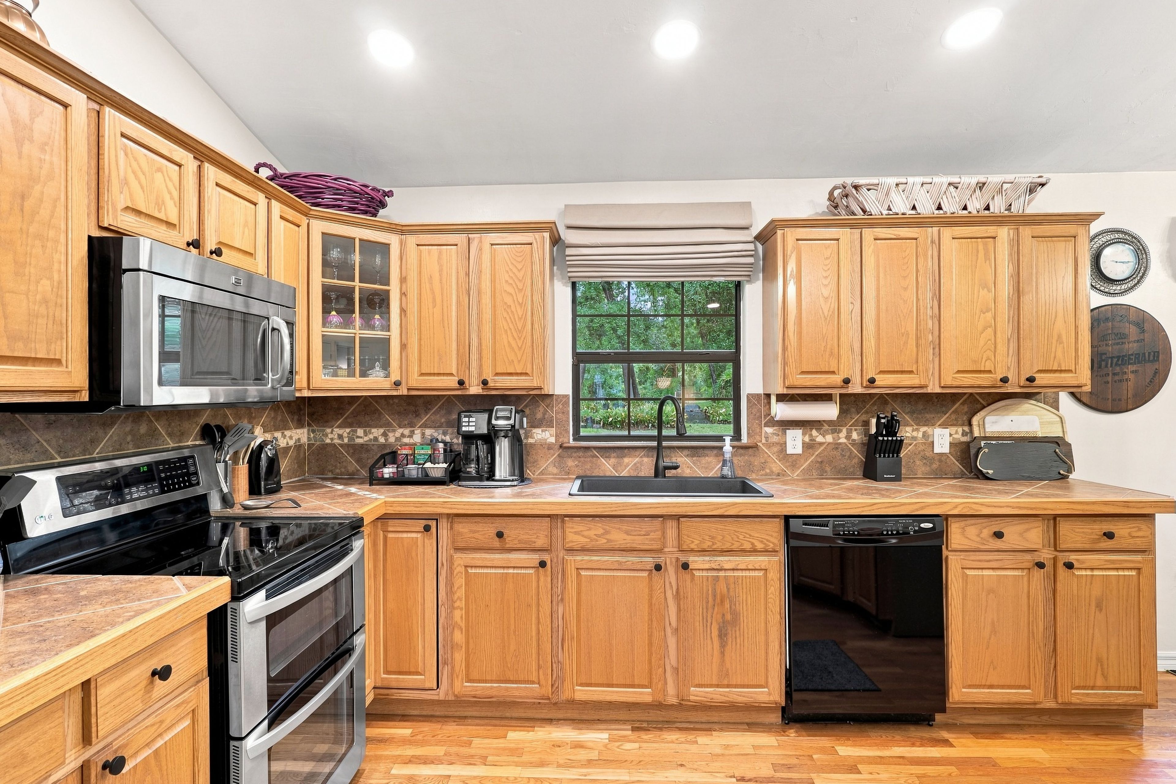 A kitchen with wooden cabinets, stainless steel appliances, a window with a view, and a clock on the wall.