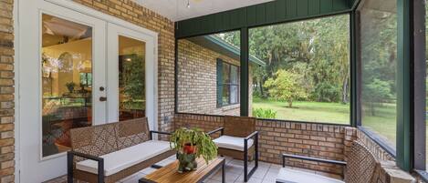 A covered patio with brick walls, a ceiling fan, and a view of a garden.