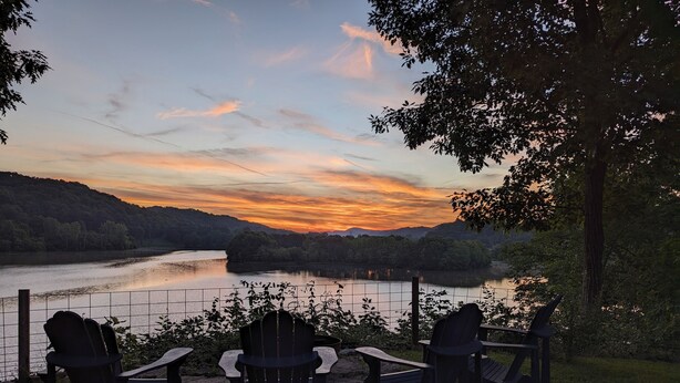 A lakeside view with chairs facing the water, surrounded by trees and hills. - Osprey Bluff, Conveniently located with exceptional sunrises and lake views. (Clinton)