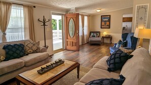 A living room with a sofa, armchair, coffee table, and a door leading to a balcony. - Osprey Bluff, Conveniently located with exceptional sunrises and lake views. (Clinton)