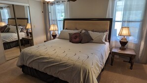 A neatly arranged bedroom with a large bed, two bedside tables with lamps, a ceiling fan, and a mirror. - Osprey Bluff, Conveniently located with exceptional sunrises and lake views. (Clinton)