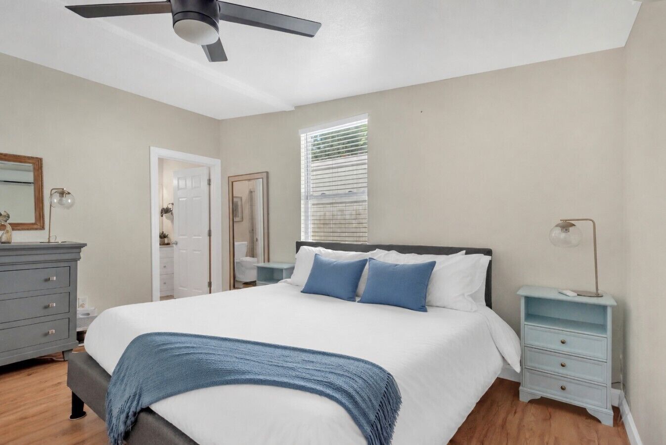 A bedroom with a bed, a dresser, a nightstand, a ceiling fan, and a window with blinds.