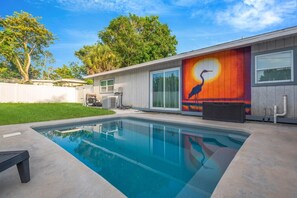 Una casa moderna con piscina, un ventanal grande y un mural con un pájaro y el sol.