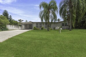 A single-story house with a covered patio, a well-maintained lawn, and mature trees.